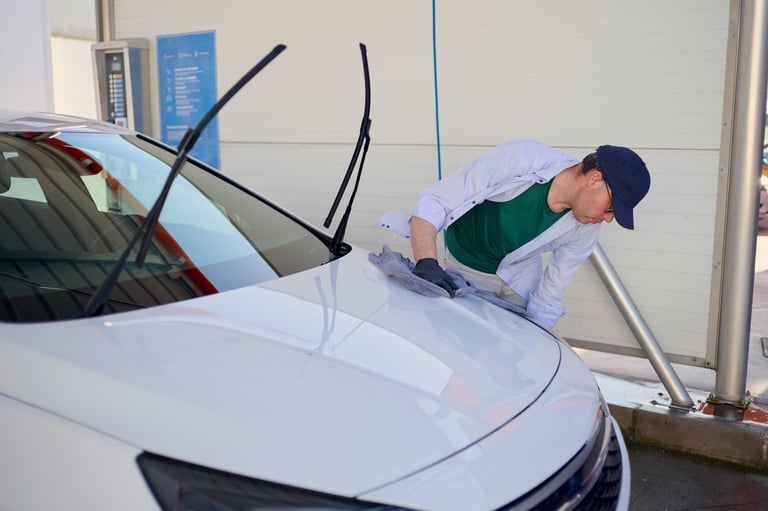 Car wash employee meticulously drying a white car hood with a microfiber cloth