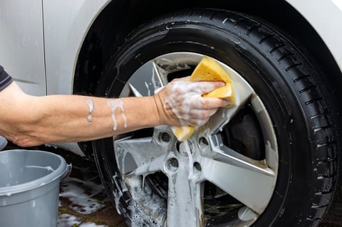 Close-up of a person's hand washing a silver alloy wheel